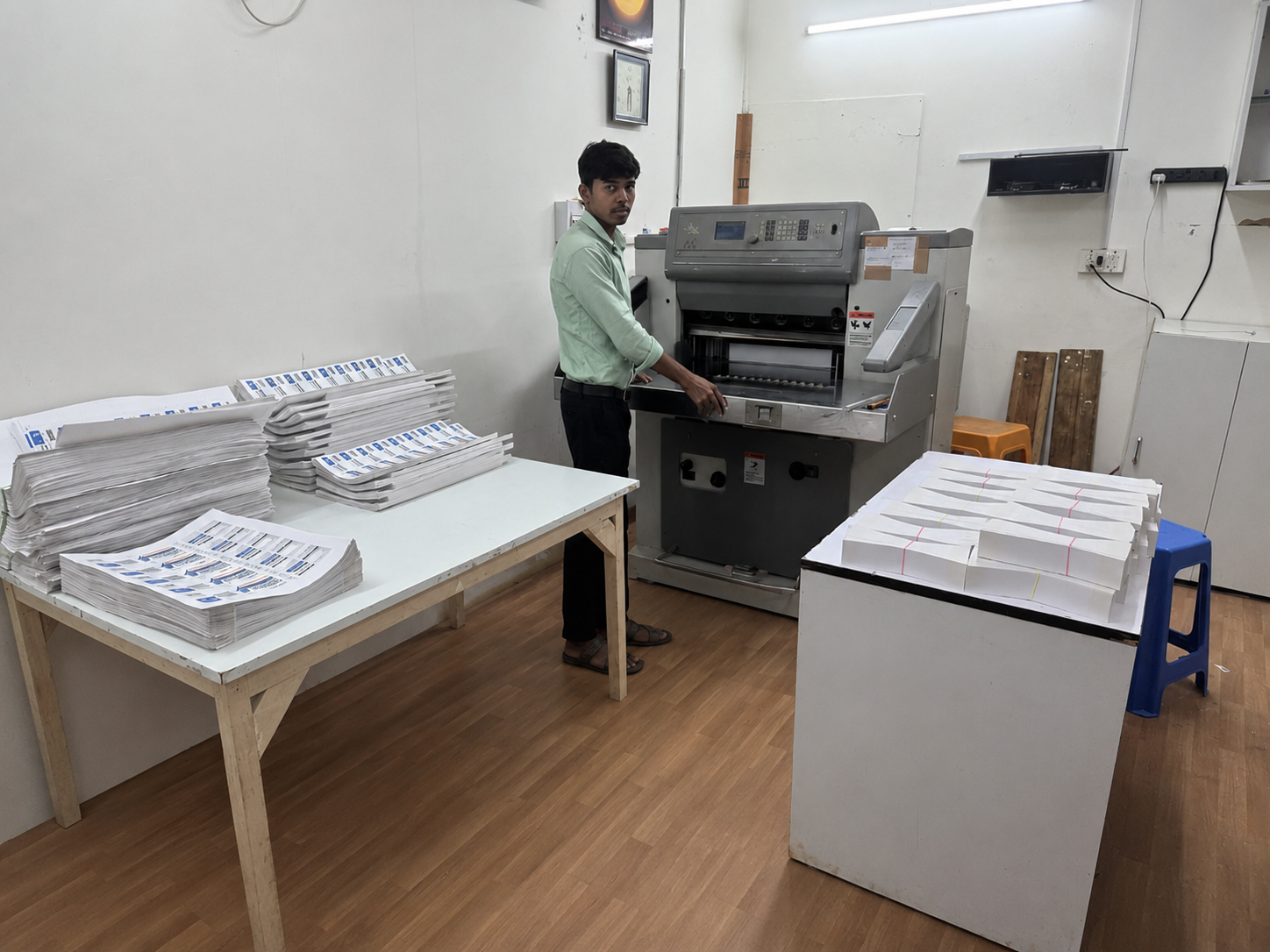Operator running the Polar paper cutting machine with stacks of printed sheets